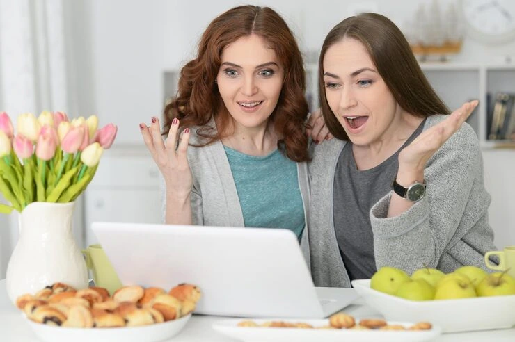 Two excited women looking at a laptop screen during a fundraising event promotion