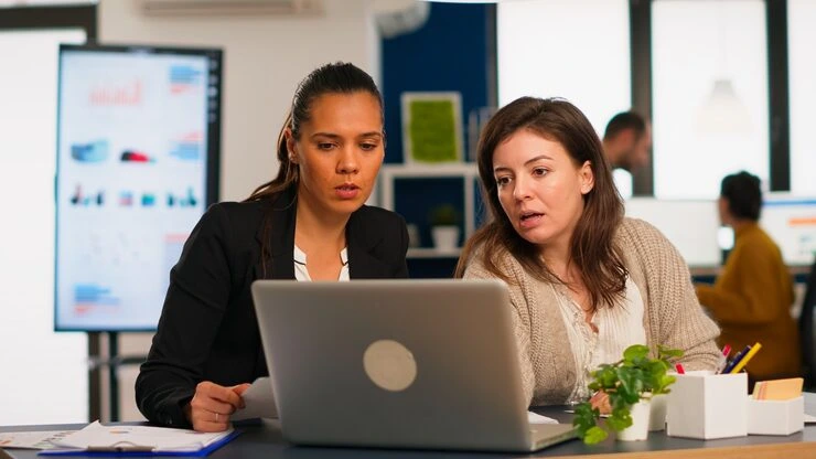 Two women reviewing telemarketing scripts and campaign execution on a laptop in an office