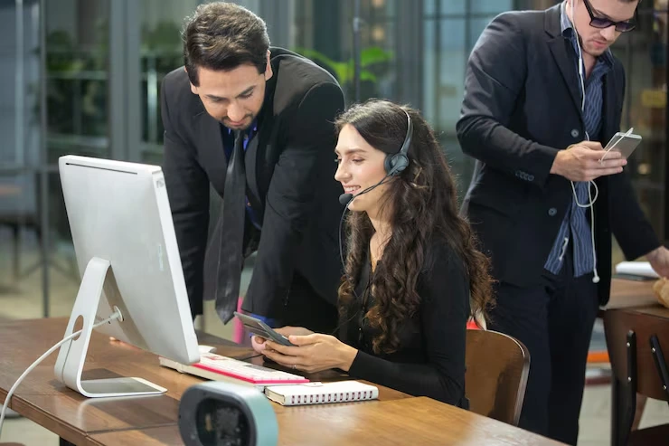 A telemarketer wearing a headset working on a computer with colleagues in an office